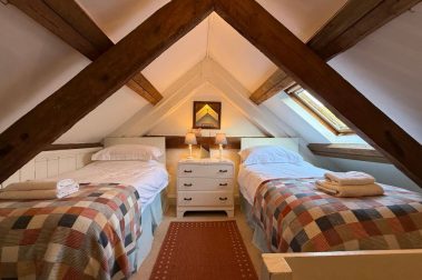 The twin bedroom above the kitchen area has a sloping beamed ceiling and is accessed by open stairs that rise directly from the kitchen.