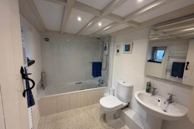 The bathroom has a toilet and wash handbasin. There is a bath with electric shower above.’